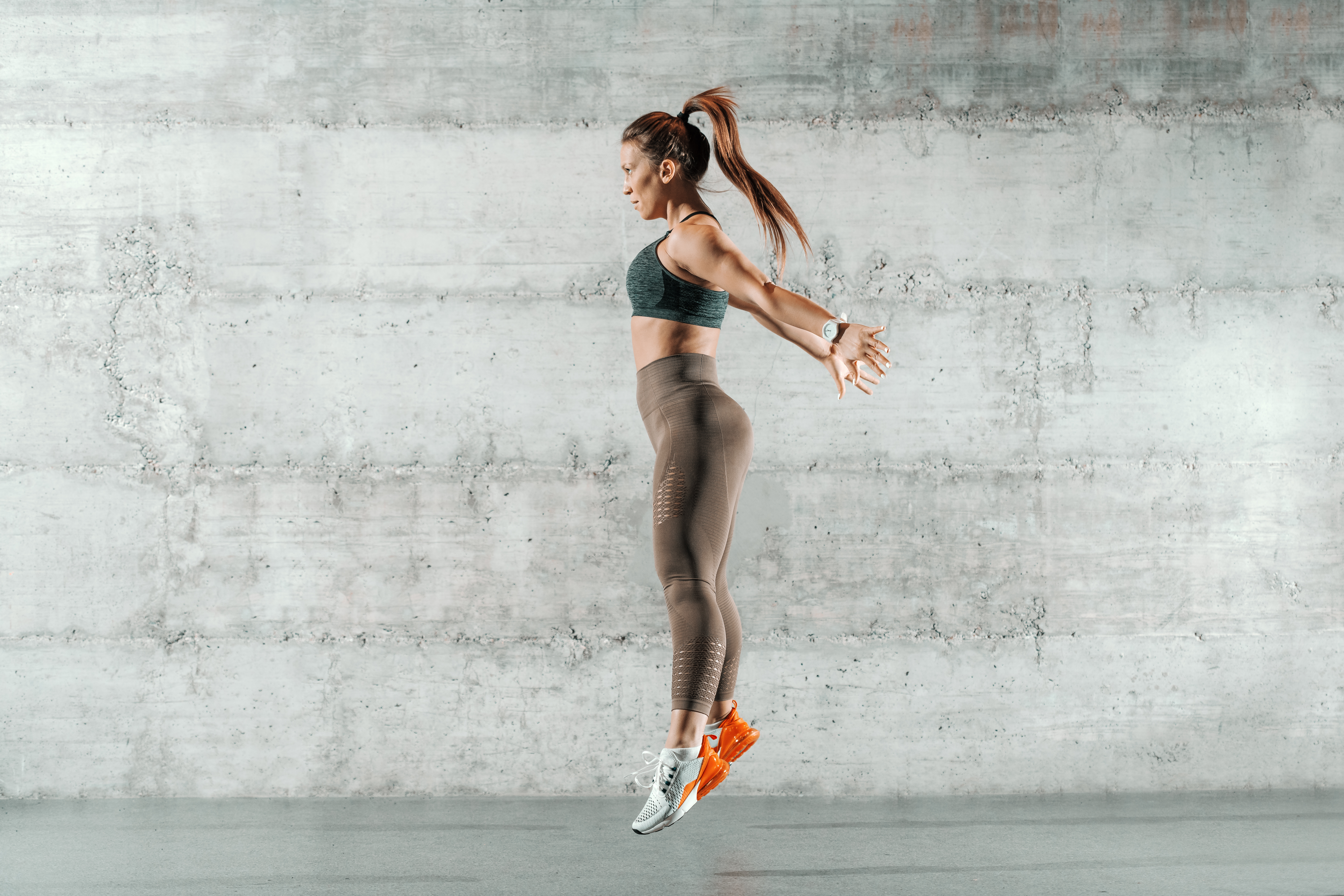Powerful Plyos You Can Do Anywhere Sporty woman doing plyometric exercise jump in front of a white wall