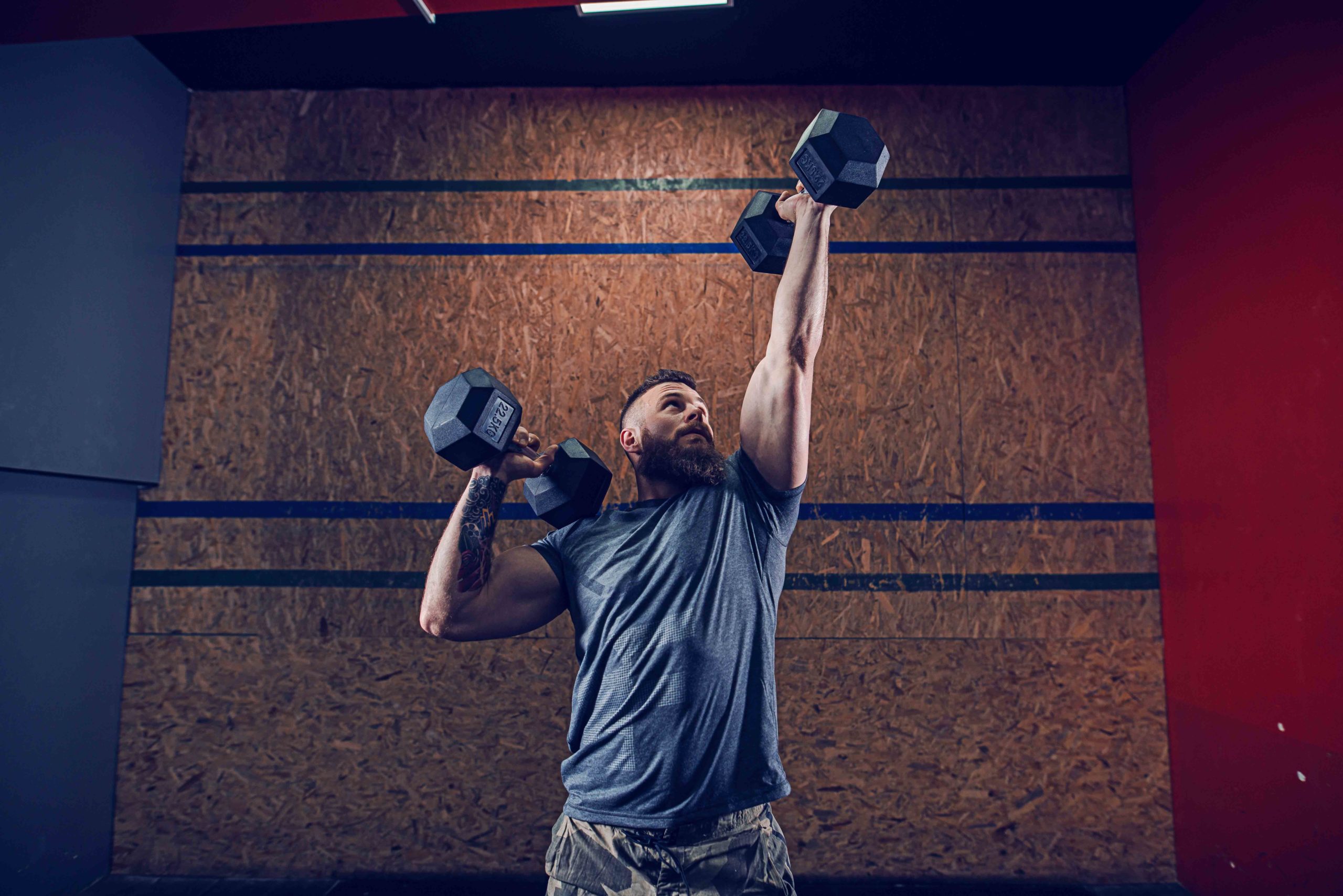 Handsome muscular man in t-shirt lifting dumbbells in the air an Strongman Overhead Press