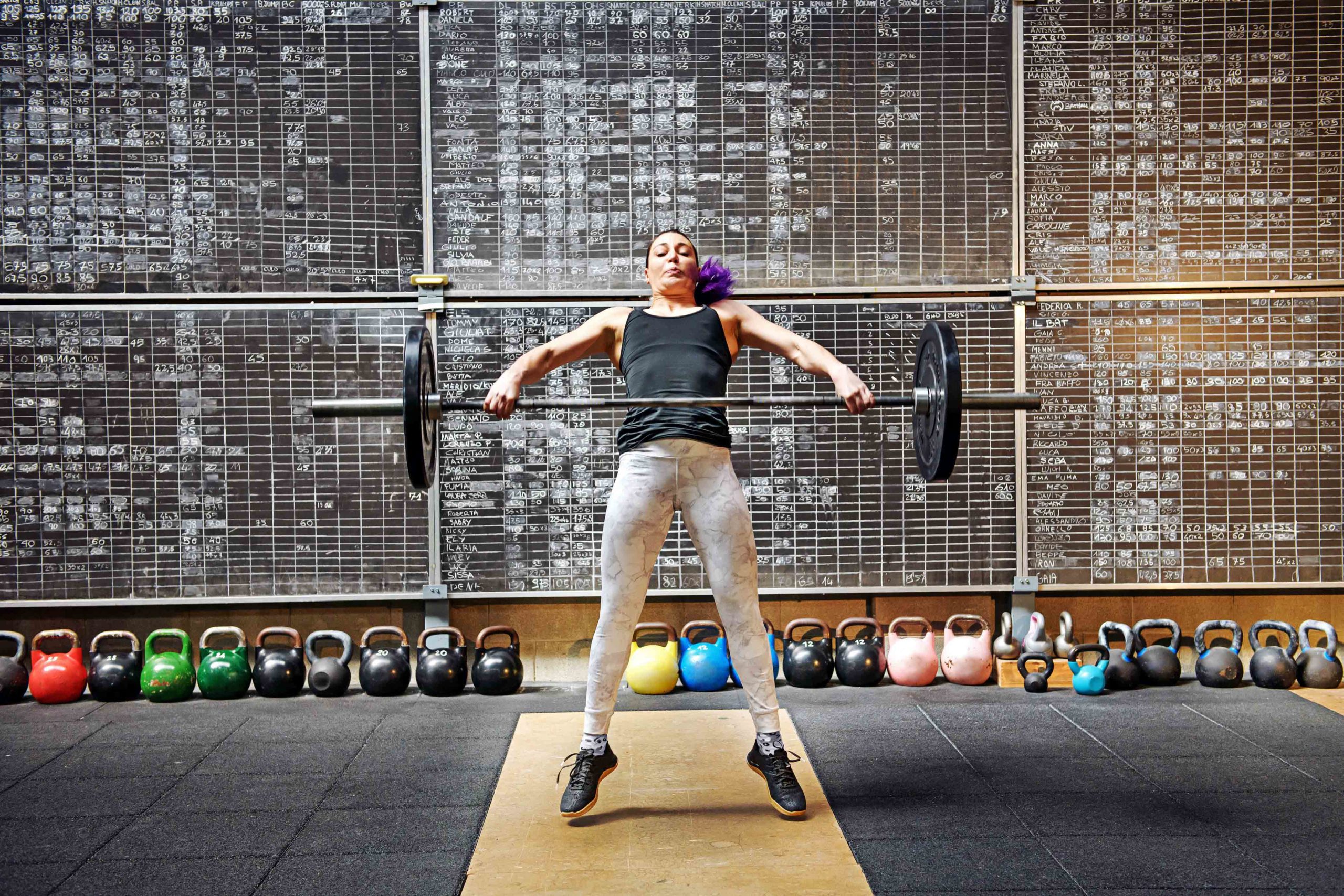 Improve Your Speed Under the Bar Woman athlete doing the snatch with a barbell snatching it off the ground to lift it above her head in a single movement seen straining with effort as she raises the weight