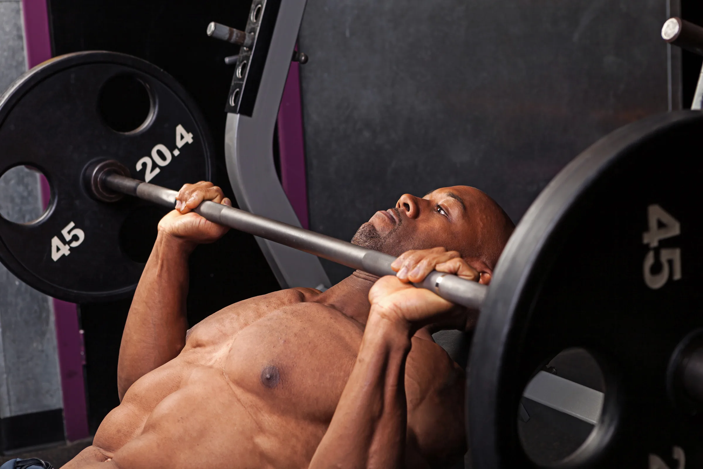 Incline Bench Pressing Professional athlete sits with a barbell on his shoulders and prepares to back squat. View from the back.