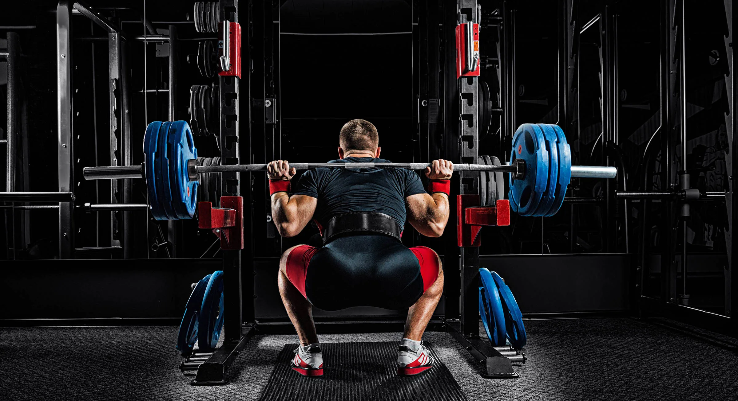 Perfect Your Back Squat Form Professional athlete sits with a barbell on his shoulders and prepares to back squat. View from the back.