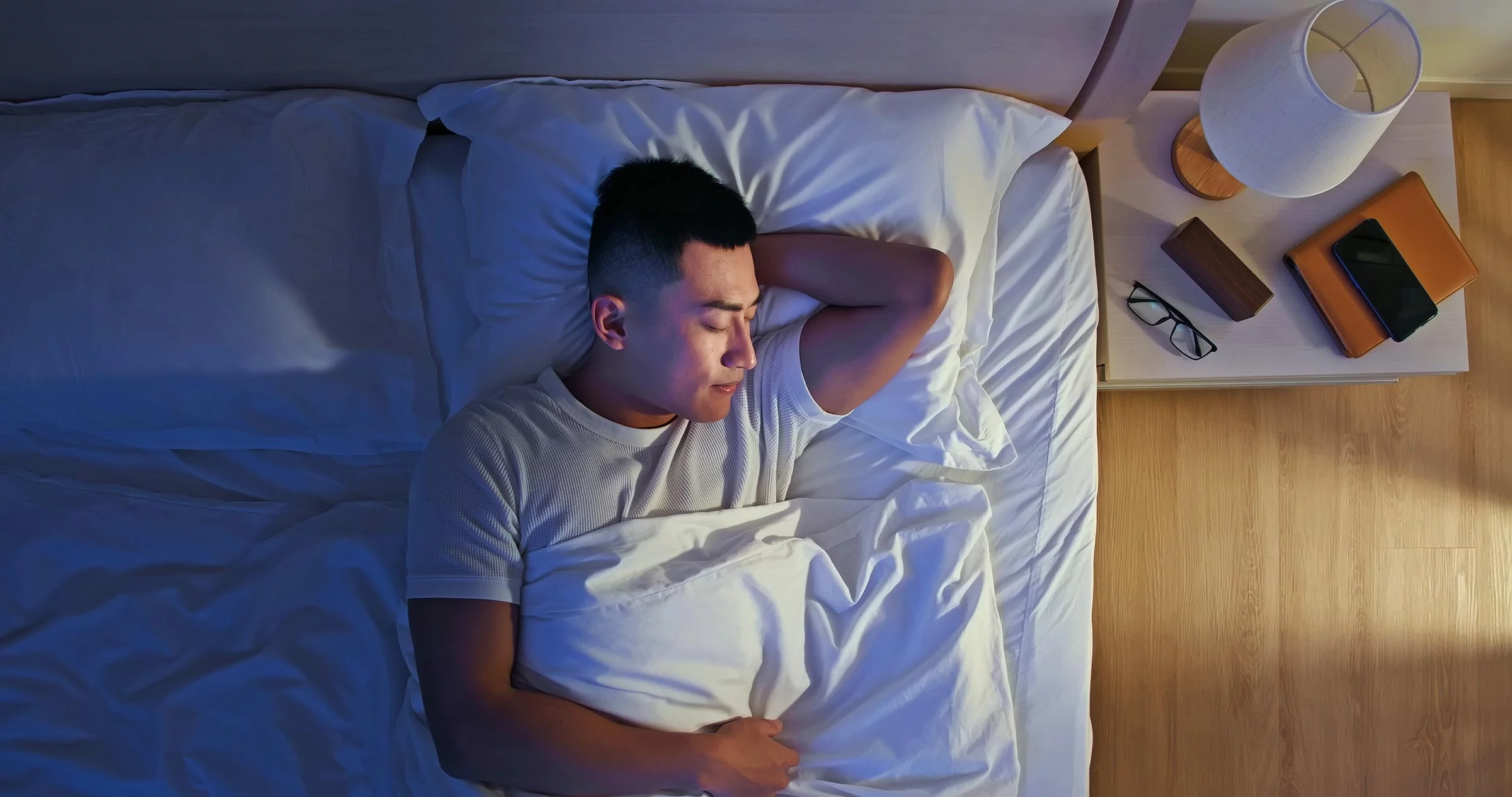 5 Strategies for Better Sleep Overhead view of man sleeping well in a bed with smile at night.